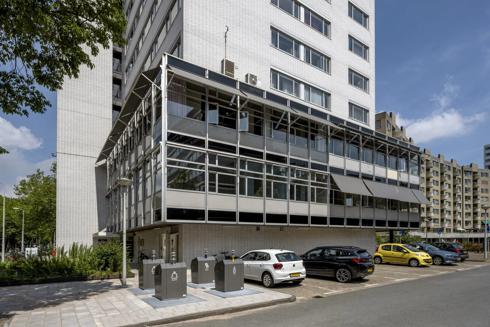 Moderne witte kantoorgebouw aan de Van Leijenberghlaan met parkeerplaatsen en ondergrondse afvalcontainers op de voorgrond.